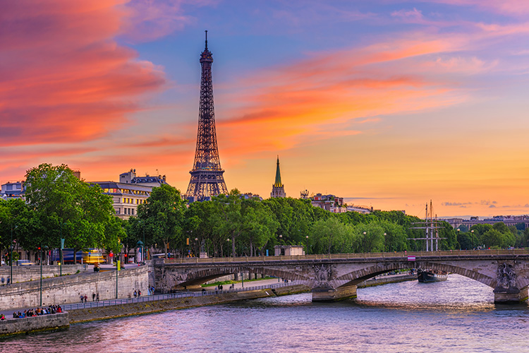Vista de un atardecer con tonos rosados. El río Sena, unos árboles verdes y de fondo, la torre Eiffel de París.